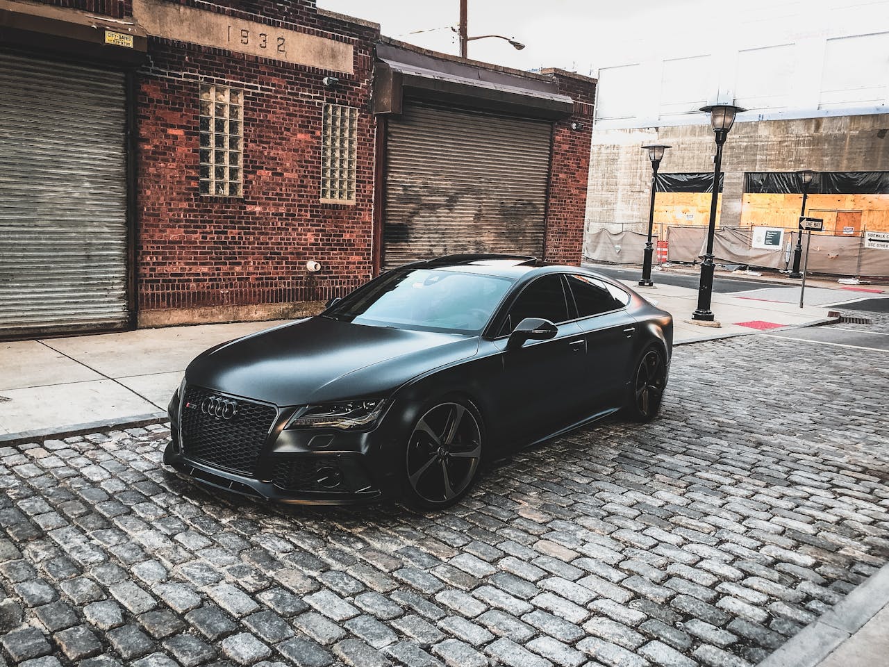 pexels-photo-909907 A sleek black car parked on a cobblestone street in an urban setting, featuring brick buildings.